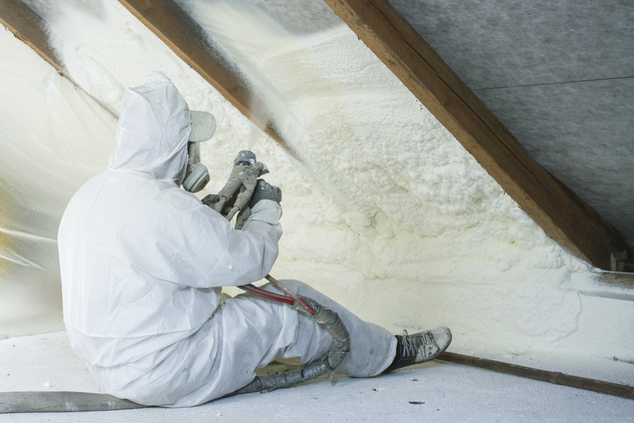 Arbeiter mit Schutzmaske bei der Sprühschaumisolierung am Dachboden